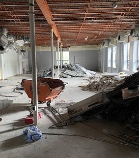 A demolition photo of the Sports Product Management space shows construction rubble piled around the space. Walls have been removed to create a bigger space. A wheelbarrow and other tools are in the center of the room. 