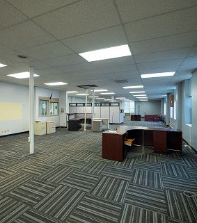 Before photo of what will be part of the Sports Product Management space. It is an office space with carpet, desks and drop ceiling. 